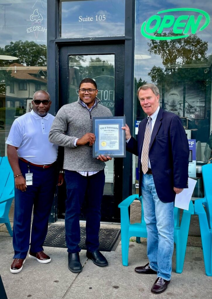 three men stand with plaque in front of glass doors