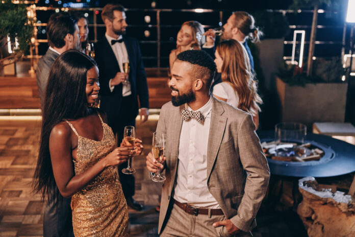 Beautiful young African couple in formalwear holding champagne flutes and smiling while spending time with friends on night party. (Photo/Getty Images)